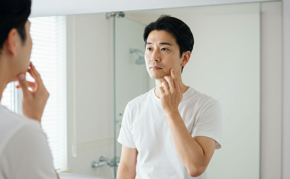 50代の男性が鏡の前で肌の状態を確認している